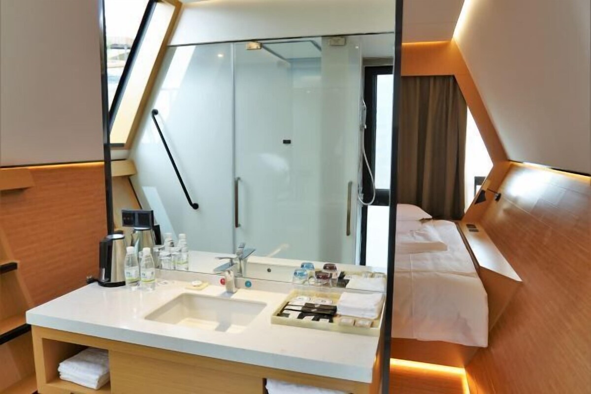Ein Hotelzimmer mit großem Spiegel, Waschbecken, Nachttisch und Bett.