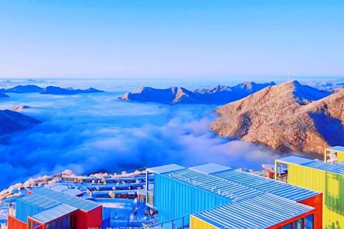 A coastal area with colorful shipping containers arranged in a semi-circular formation, overlooking a mountainous landscape and the sea.