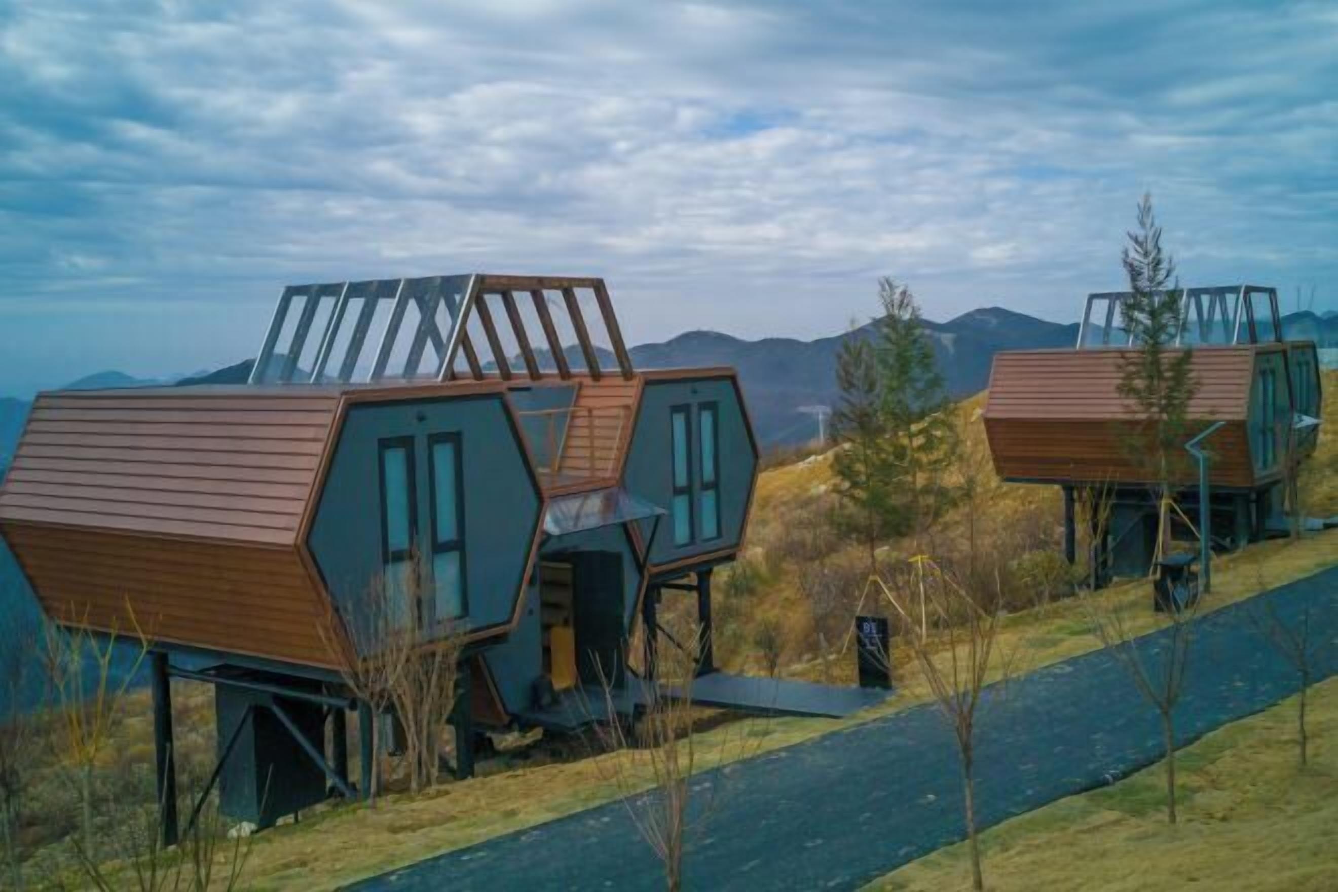 Una serie de cabañas hexagonales con techos de madera y ventanas amplias, con montañas al fondo.