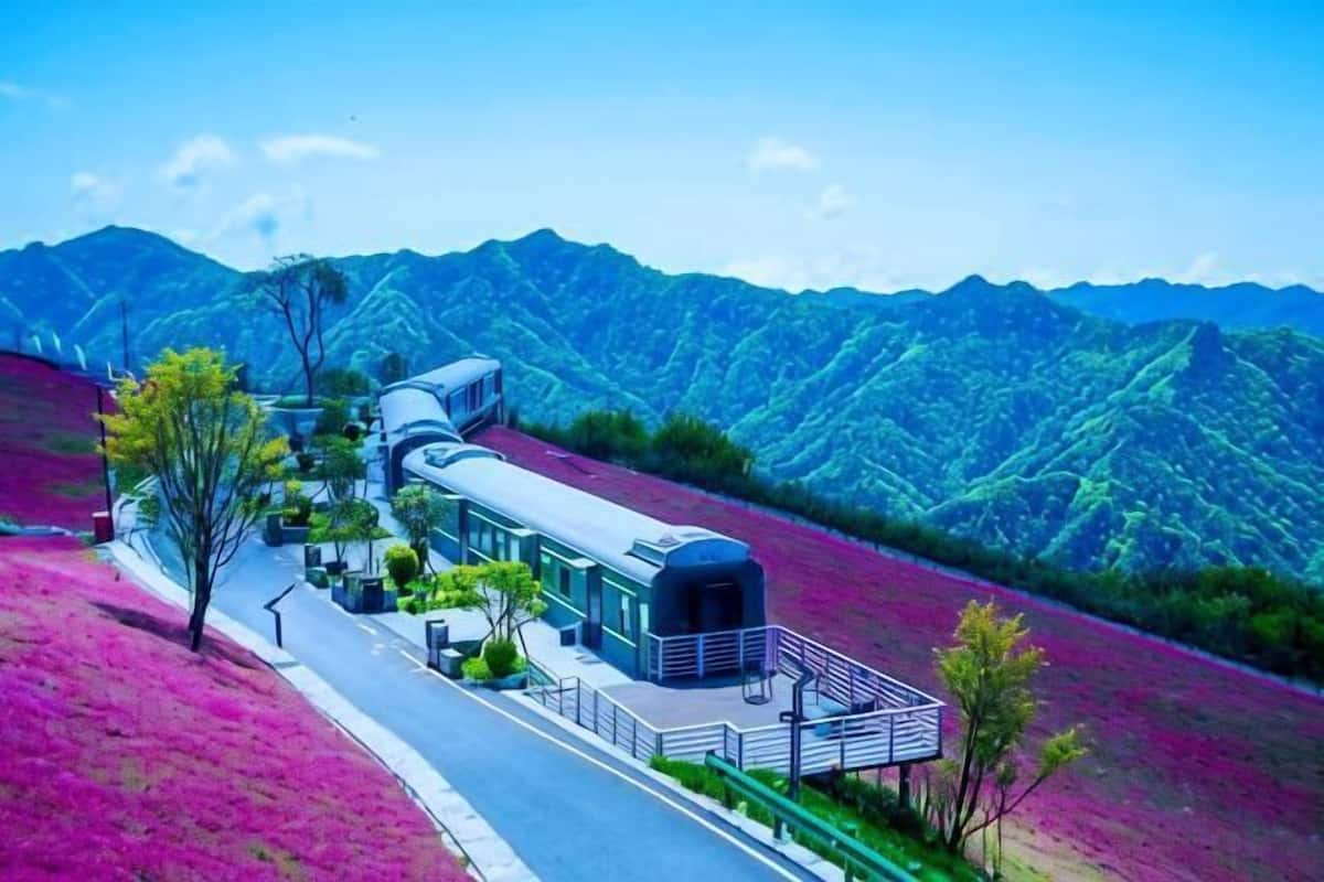 A modern building with a curved structure, surrounded by a road and greenery, set against a mountainous backdrop.