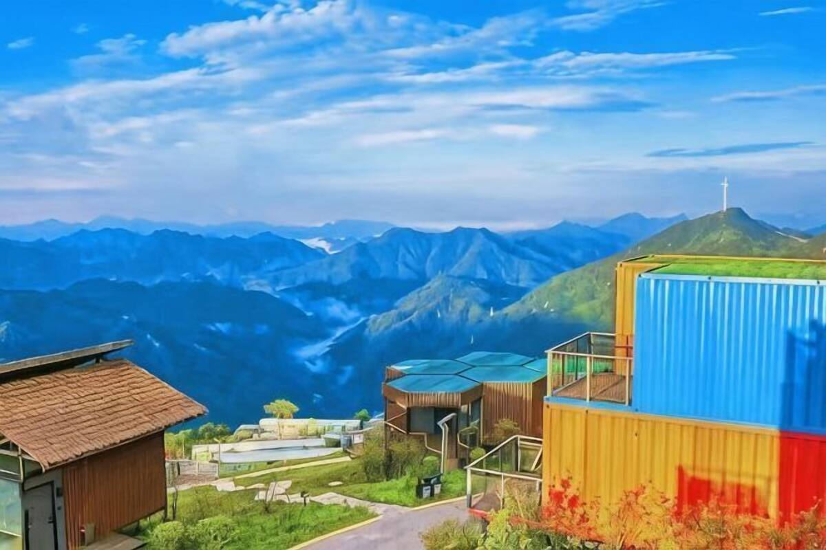 A mountainous landscape with buildings, including a structure with a green roof and a blue container.