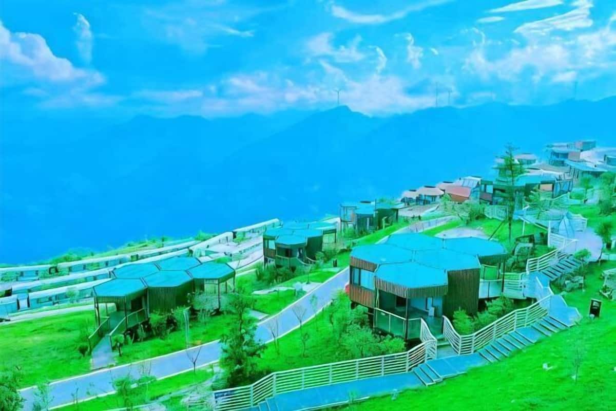 A hillside resort with multiple buildings, a winding road, and a view of the ocean.