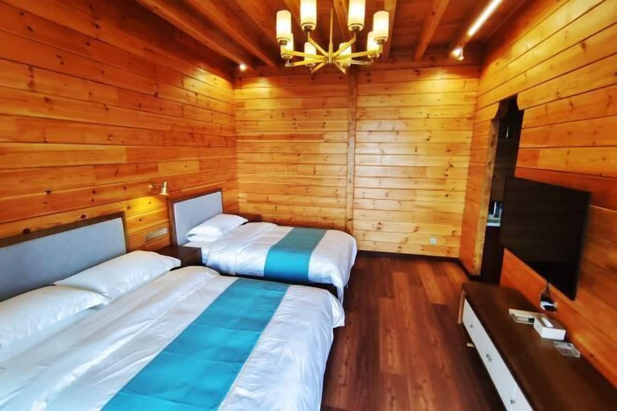 A wooden cabin room with two beds, a TV, and a wooden ceiling.