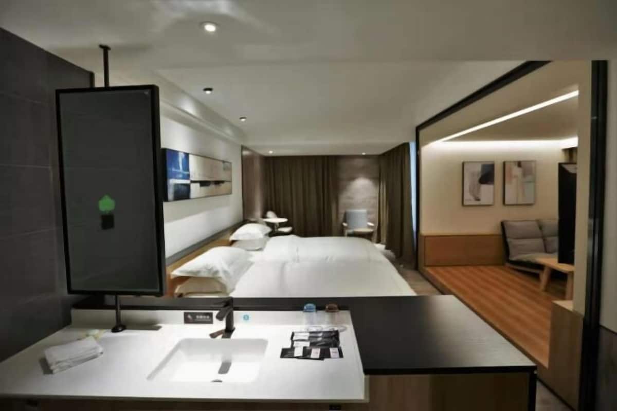 A hotel room with a bed, bedside table, and a bathroom with a sink and mirror.