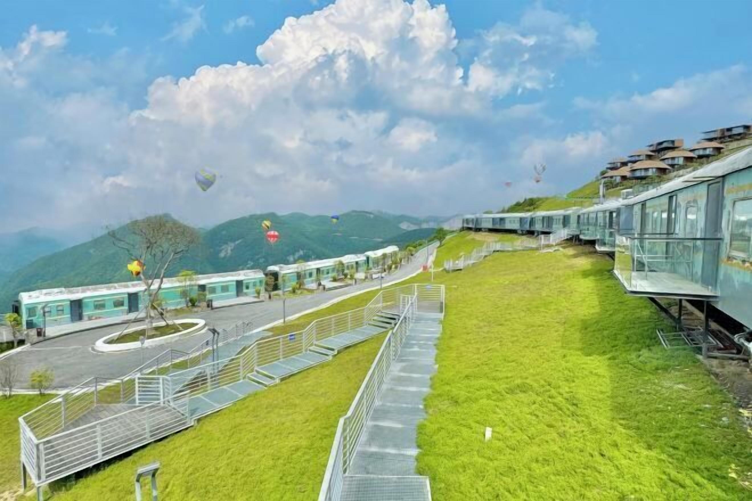A modern building with a glass facade, a grassy area in front, and a train track running alongside.