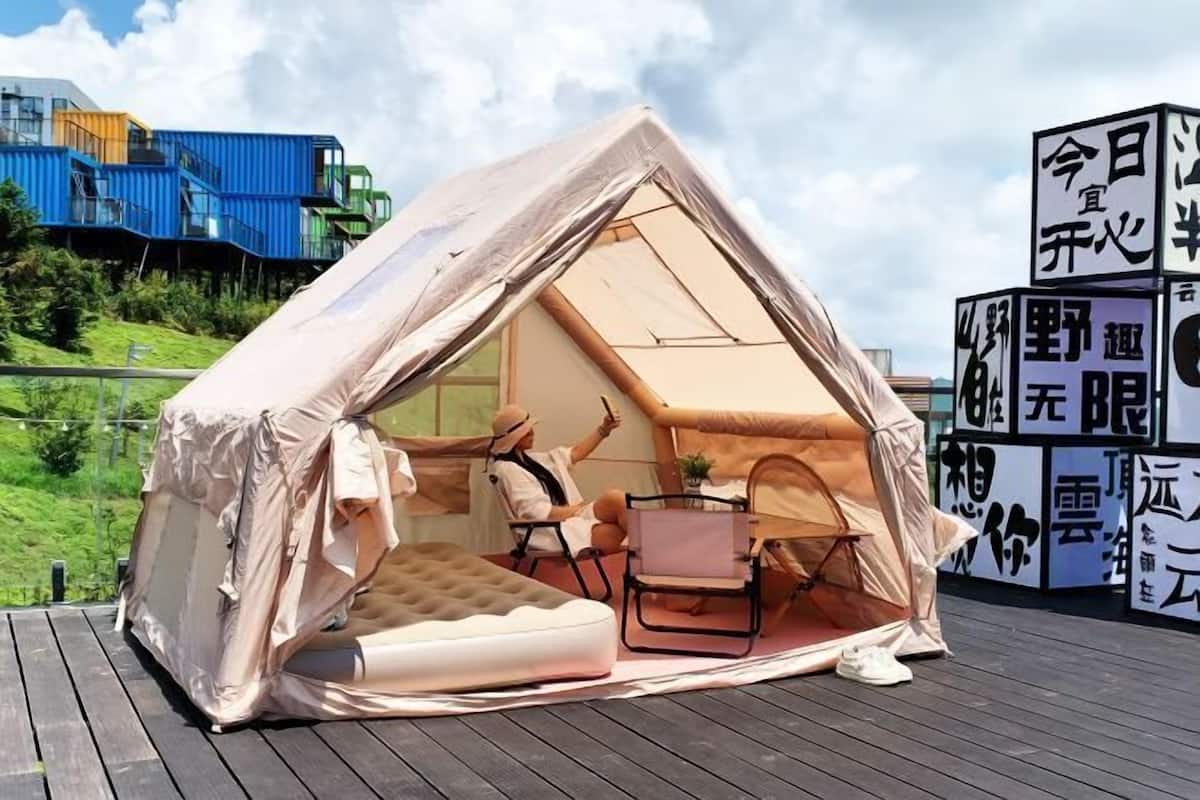 A tent-like structure with a mattress and a chair inside, set on a wooden deck.