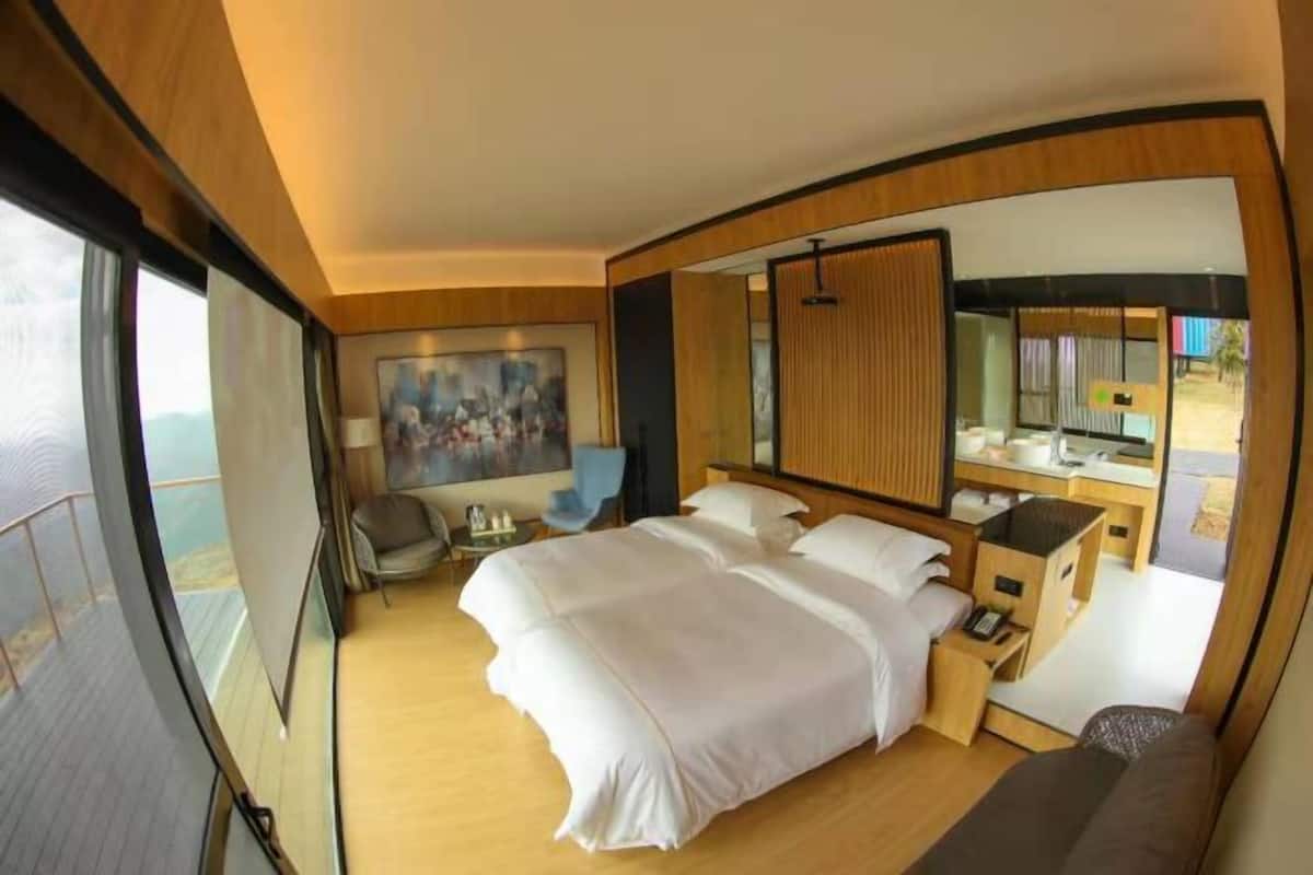 A hotel room with a large bed, a desk, a chair, and a large window.