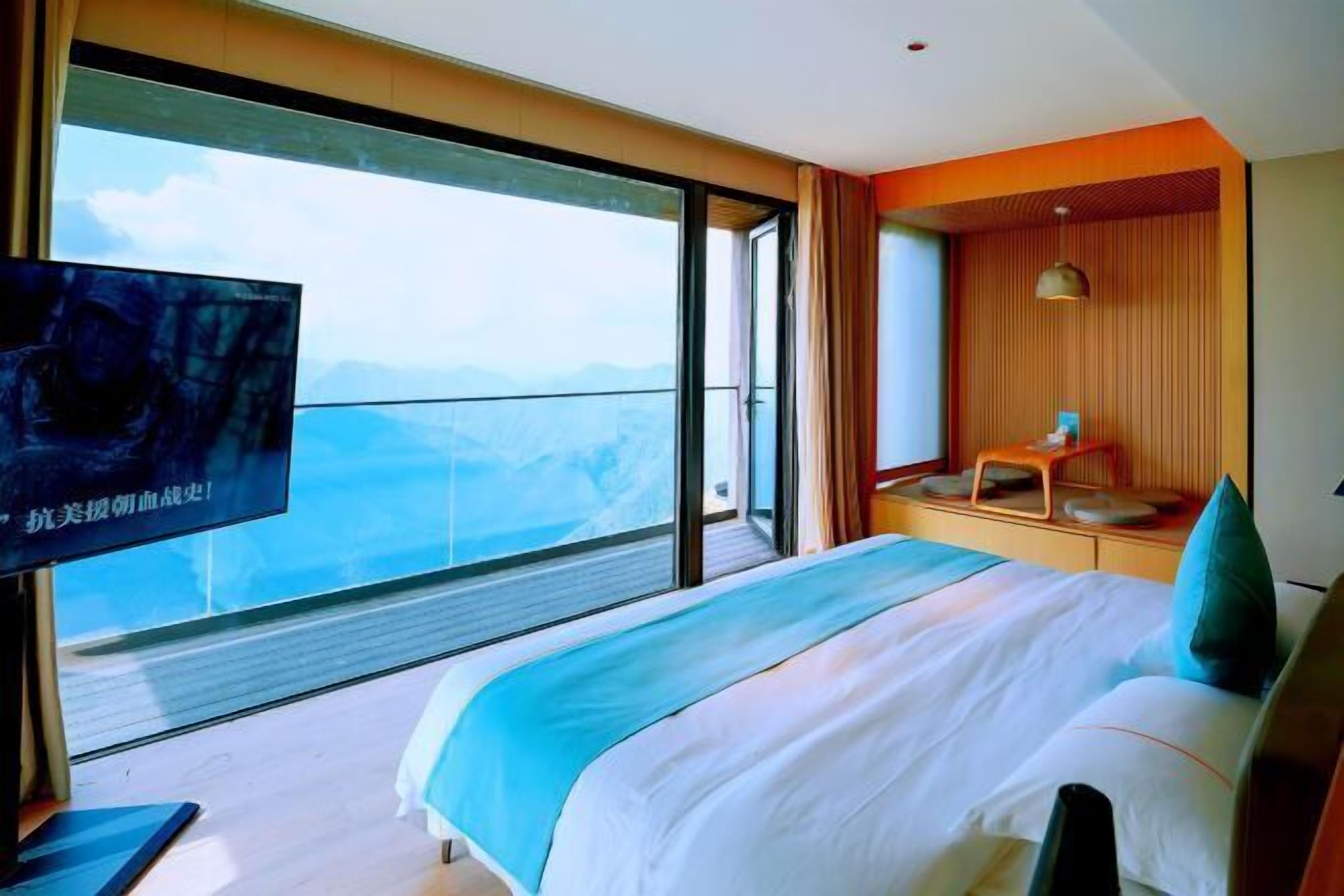 A hotel room with a large bed, a television, and a balcony with a view of the mountains.