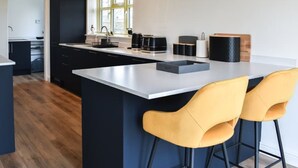 A modern kitchen with a large island, black cabinets, and yellow bar stools. - Spacious and modern 4 bedroomed detached house with panoramic views (Holyhead)