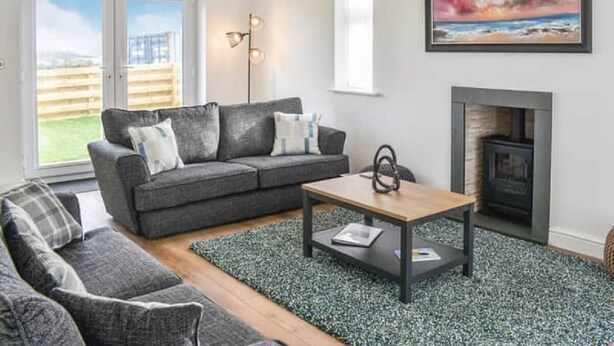 A modern living room with a grey sofa, a wooden coffee table, and a fireplace. - Spacious and modern 4 bedroomed detached house with panoramic views (Holyhead)