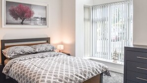 A bedroom with a bed, a bedside table with a lamp, a window with blinds, and a framed picture on the wall. - Spacious and modern 4 bedroomed detached house with panoramic views (Holyhead)