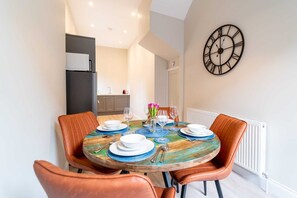 Un coin repas avec une table ronde, des chaises orange et une horloge murale.