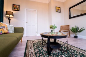Un salon avec un canapé vert, une table basse ronde sur laquelle se trouve un vase, une porte et un miroir accroché au mur.
