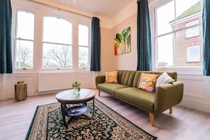 A living room with a sofa, a coffee table, a patterned rug, and large windows with curtains.
