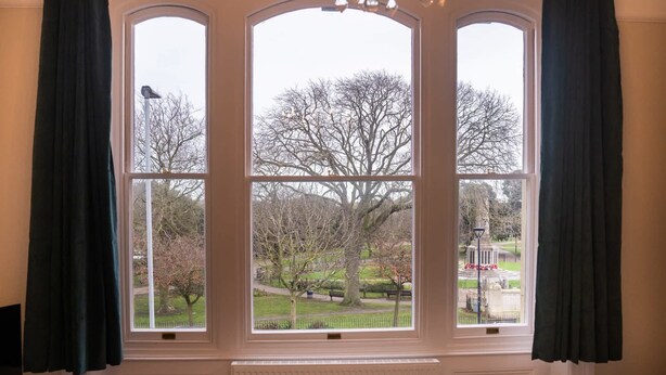 A room with a large window featuring three panes, dark curtains, and a chandelier.