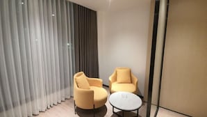 Ein modernes Zimmer mit zwei gelben Sesseln, einem kleinen weißen Tisch und einem großen Fenster mit durchsichtigen Vorhängen.