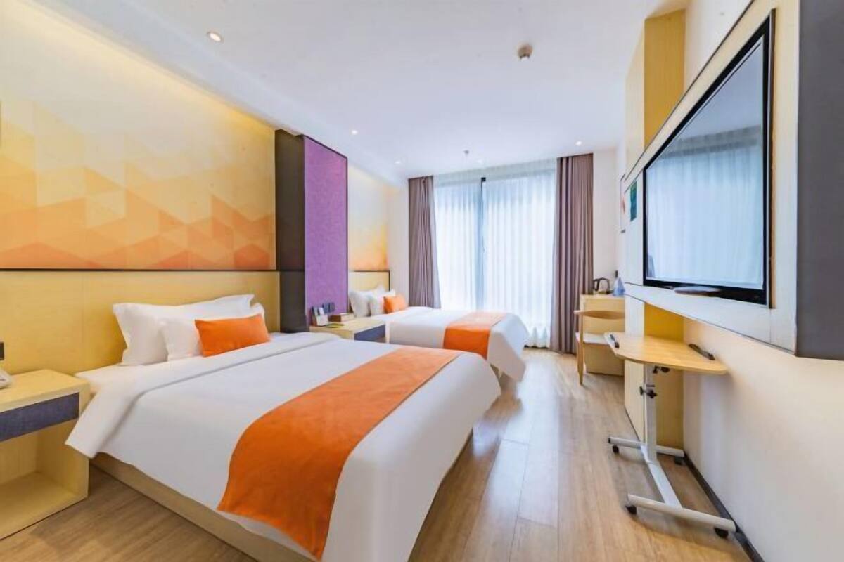 Une chambre d’hôtel avec deux lits, un bureau, une télévision et une grande fenêtre avec des rideaux.