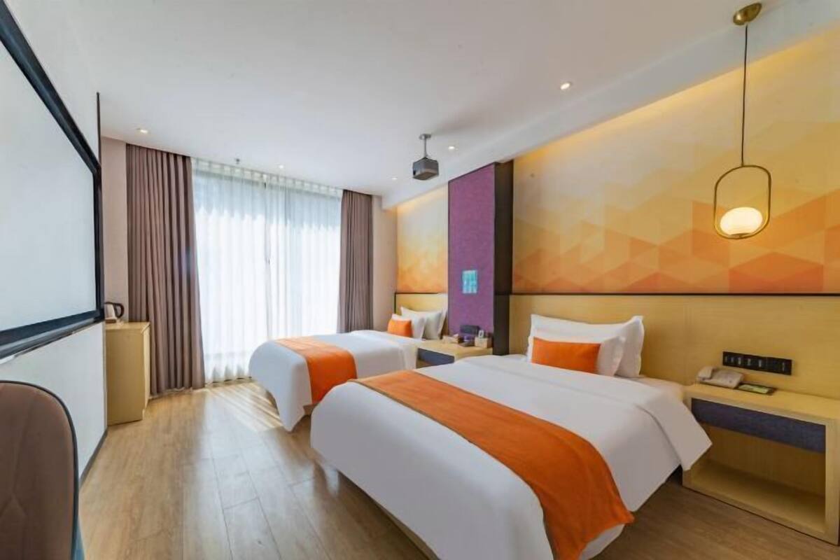 Une chambre d’hôtel avec deux lits, un bureau, une chaise et une grande fenêtre avec des rideaux.