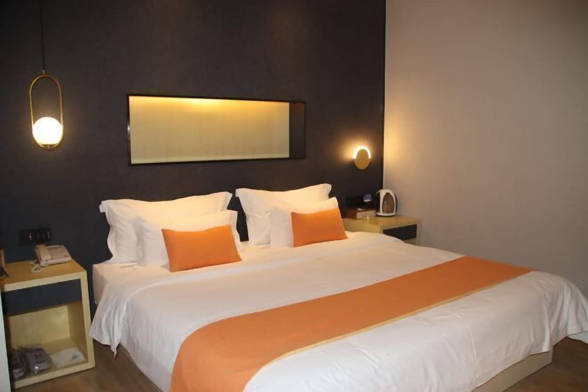 A hotel room with a large bed, two bedside tables, a nightstand, a wall-mounted light, and a mirror.