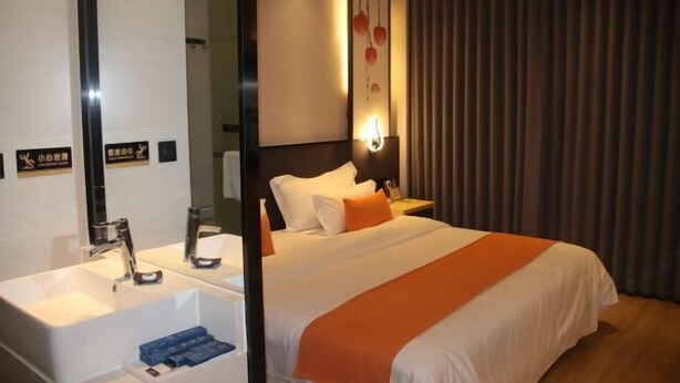 Ein Hotelzimmer mit einem großen Bett, einem Nachttisch, einem Spiegel, einer Wandleuchte und einem Vorhang.