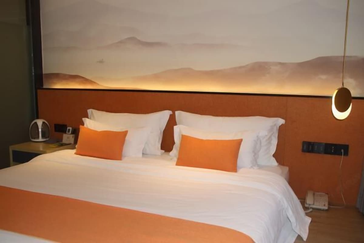 A hotel room with a large bed, two pillows, a nightstand with a phone and a lamp, and a wall-mounted light fixture.