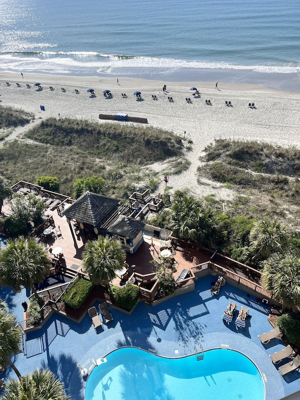A resort with a pool, beach chairs, and umbrellas.