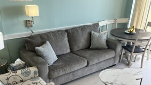 Una sala de estar con un sofá gris, un sillón estampado y una mesa redonda con sillas.