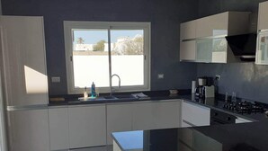 A modern kitchen with a central island, a window with a view, and built-in appliances. - Villa Sonia with infinity pool (djerba)
