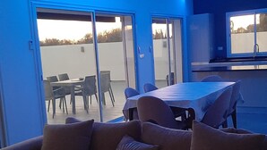 A modern living room with a sofa, a dining table, and chairs. There are large windows and a view of the outdoors. - Villa Sonia with infinity pool (djerba)