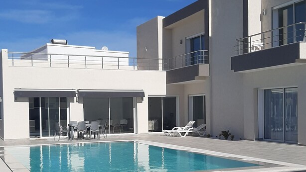 A modern building with a swimming pool, outdoor seating, and a clear blue sky. - Villa Sonia with infinity pool (djerba)