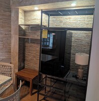 Una habitación con pared de ladrillo, un banco de madera, estante metálico y una lámpara.