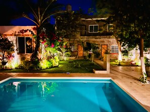 A swimming pool with a clear view of the surrounding garden and a two-story house with visible windows and doors.