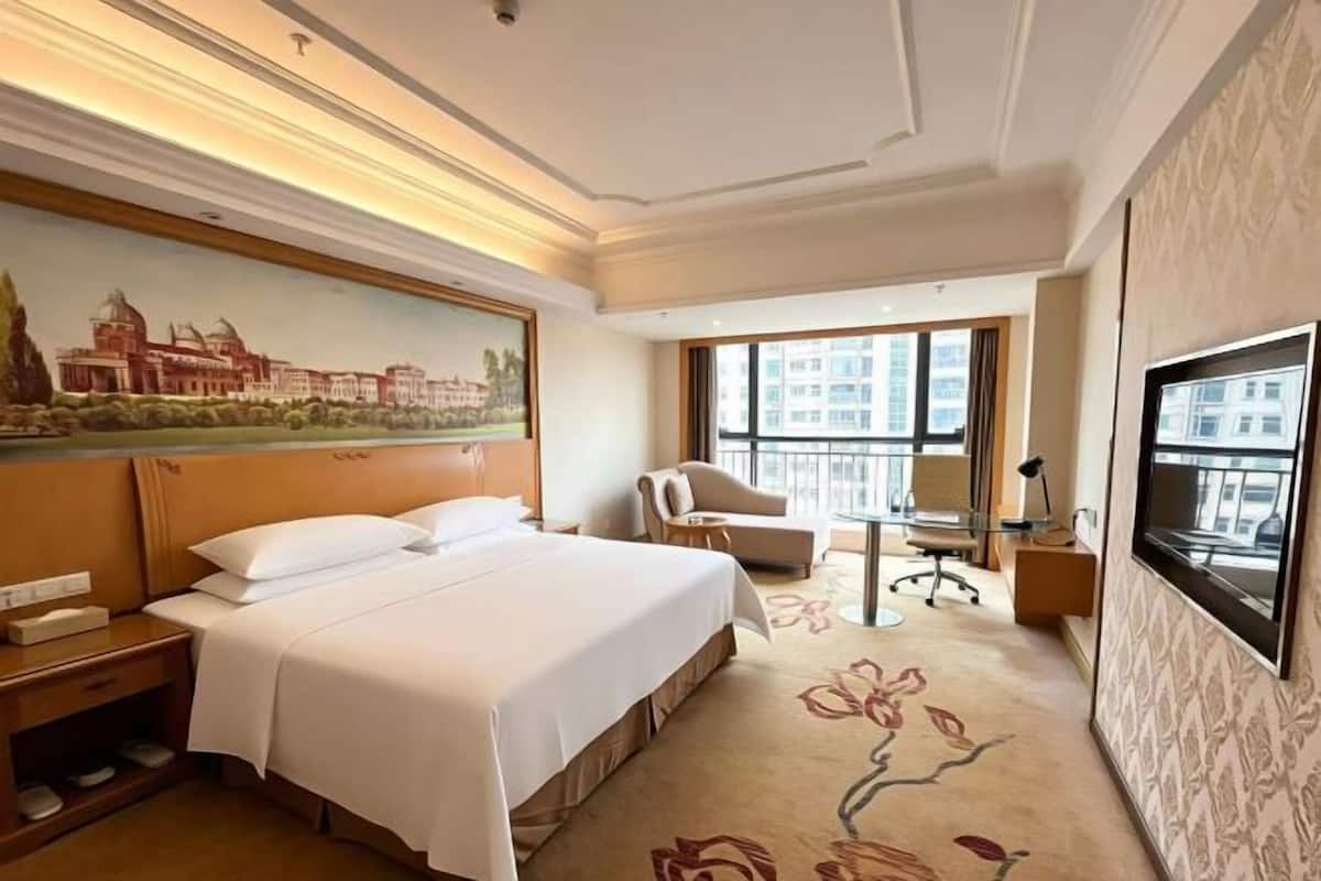 A hotel room with a bed, a desk, a chair, a TV, and a large window.
