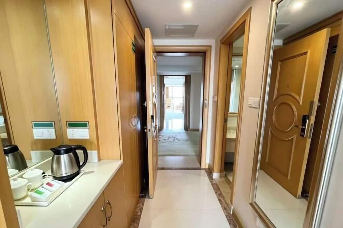 A hotel corridor with wooden doors, a coffee station, and a view into the room.