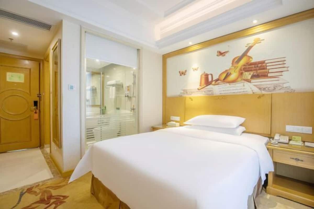 A hotel room with a large bed, a nightstand, a desk, and a wall with a mural of musical instruments and books.
