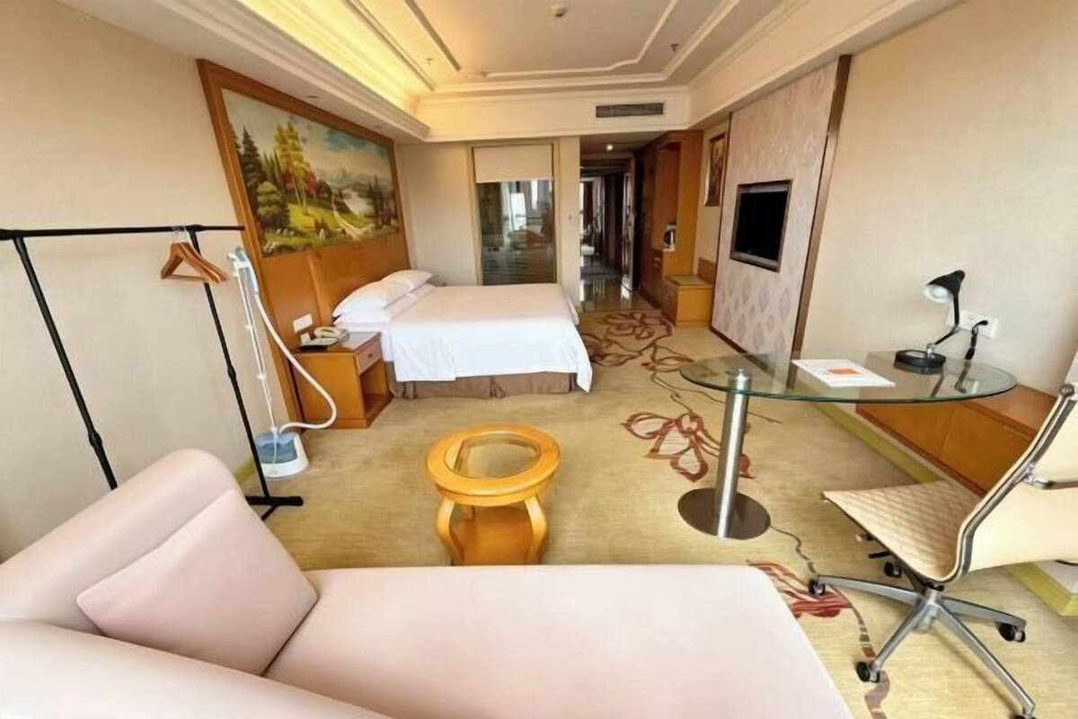 A hotel room with a bed, a desk with a chair, a toilet, and a painting on the wall.