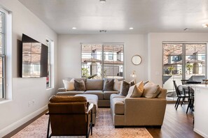 Relax in this stylish living room with a sofa, ottoman, and dining area, offering views of the surrounding cityscape.