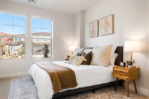 Cozy retreat with a large bed, nightstand, and artwork, set against a residential backdrop.
