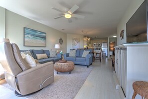A living room with a sofa, a chair, a round ottoman, and a ceiling fan.