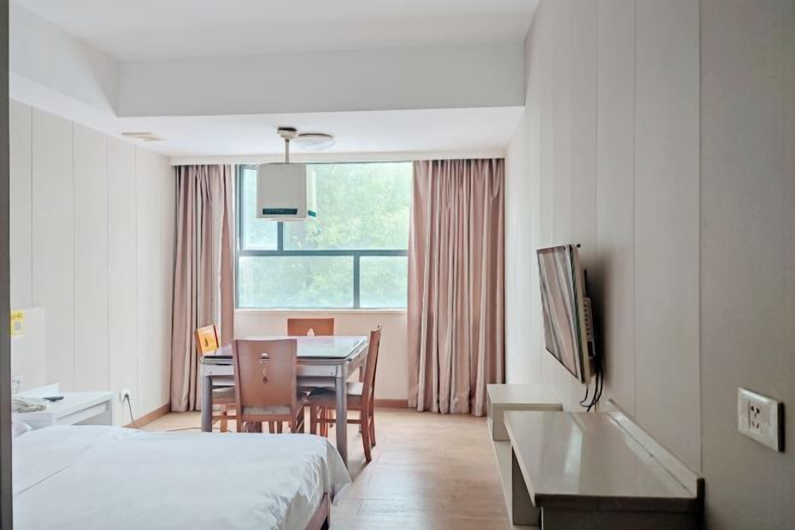 Una habitación de hotel con cama, escritorio, silla, televisor y ventana con cortinas.