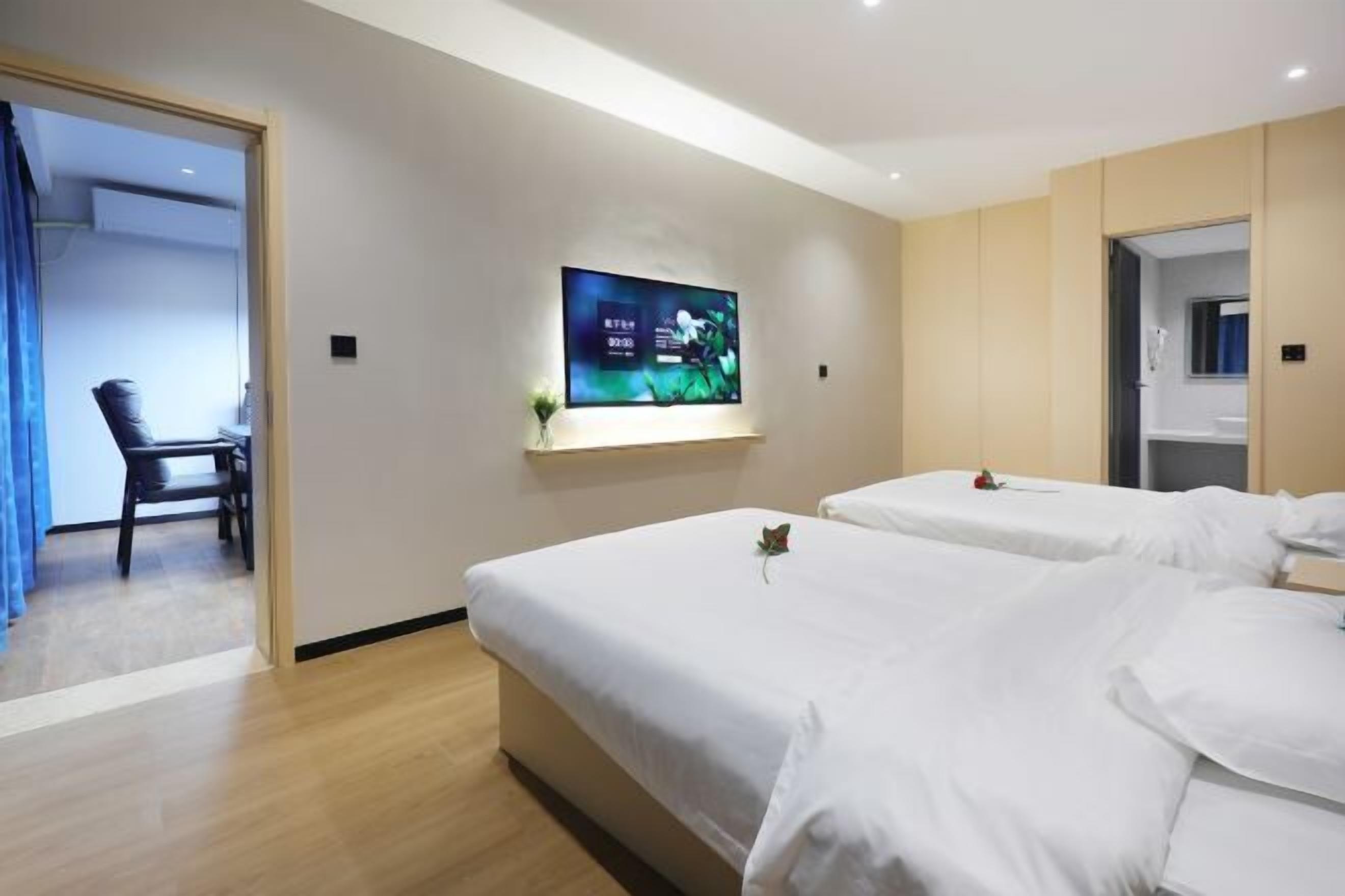 Habitación de hotel con dos camas, un televisor en la pared y una silla en la esquina.