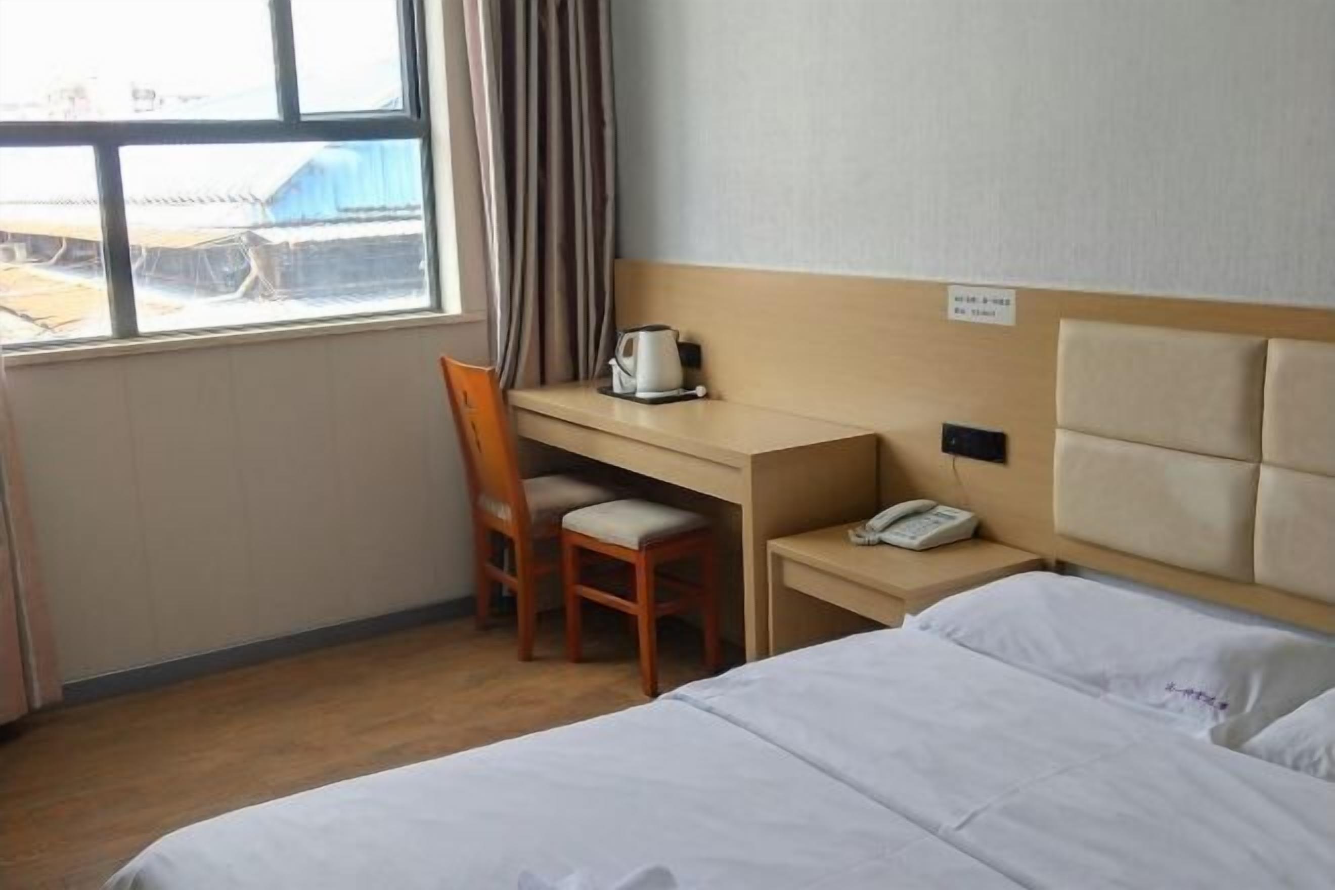 A hotel room with a bed, a desk, a chair, a telephone, and a window with curtains.