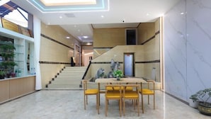 Eine großzügige Lobby mit Marmorboden, einer Treppe, einem Empfangsbereich und einem Essbereich mit gelben Stühlen.