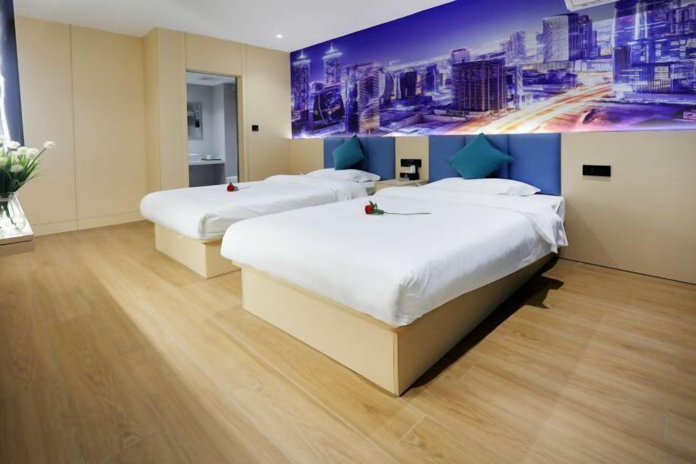 Hotellihuone, jossa on kaksi sänkyä, seinällä kaupunkimaisemaa esittävä seinämaalaus ja puulattia.