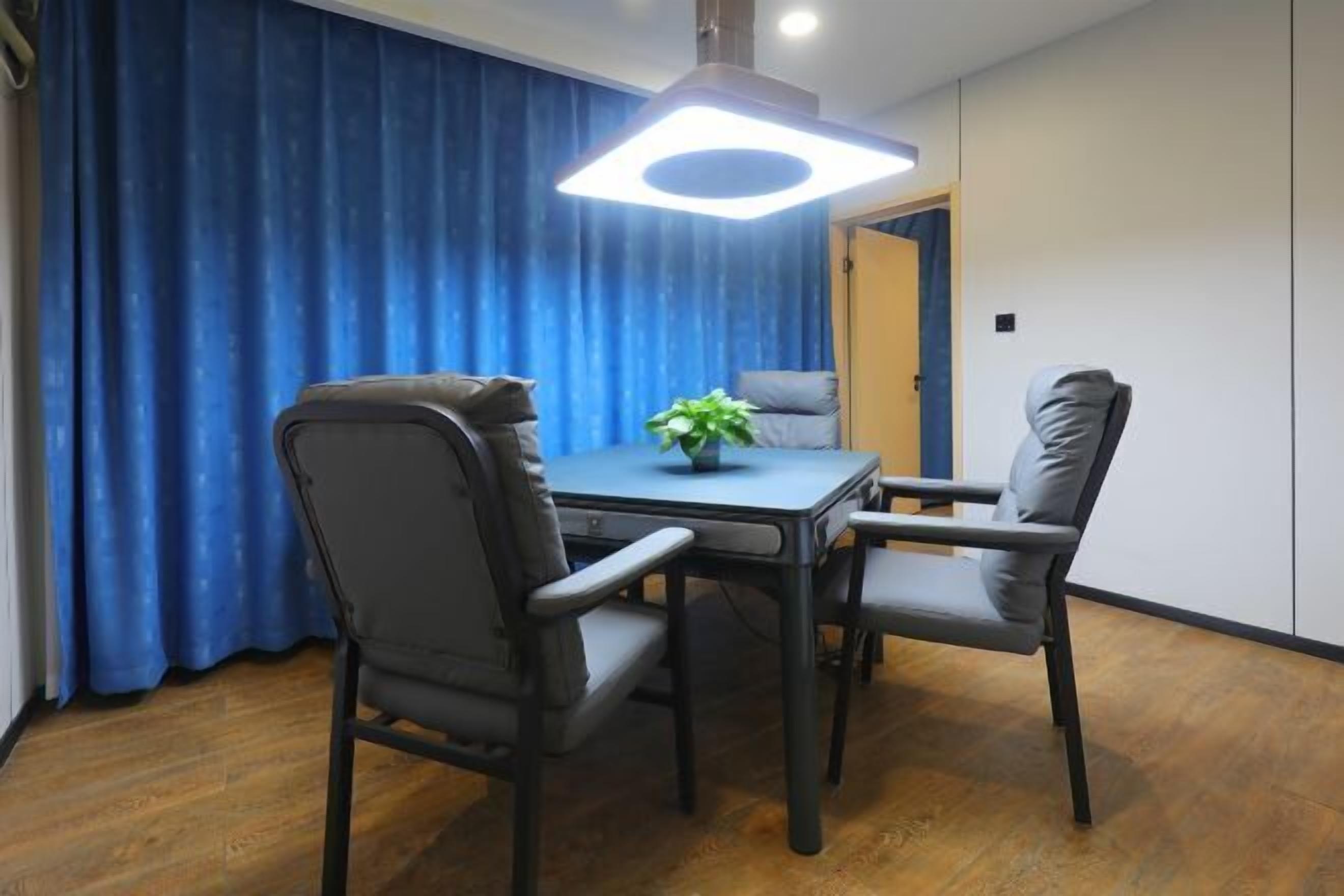 A dining area with a table and four chairs, a pendant light, and a blue curtain.