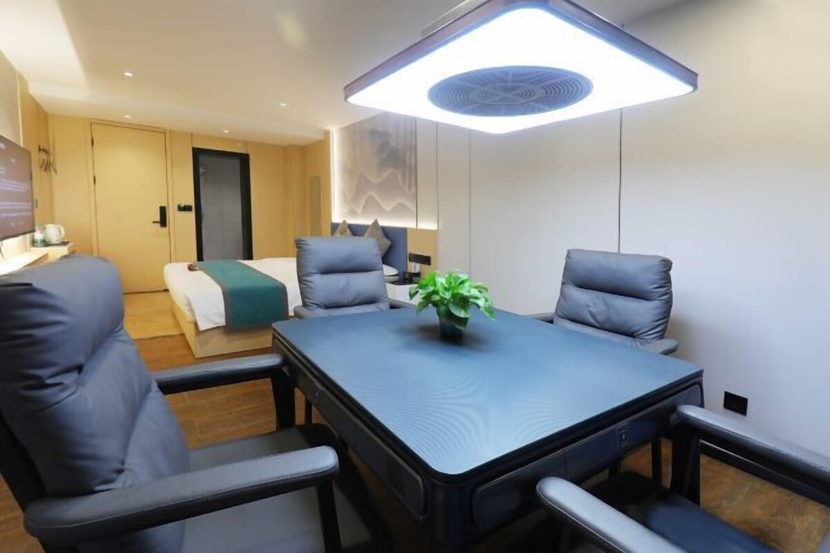 A modern hotel room with a large bed, a desk, and a conference table with chairs.