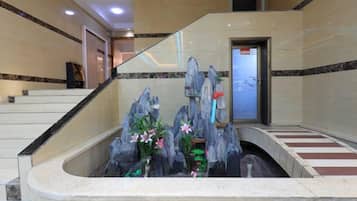 Un área de recepción con una escalera de mármol, un mostrador de recepción y una fuente decorativa de rocas.