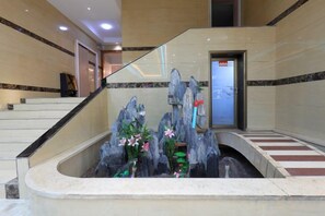 A reception area with a marble staircase, a reception desk, and a decorative rock fountain.