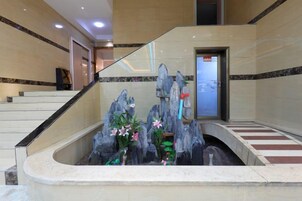 Un área de recepción con una escalera de mármol, un mostrador de recepción y una fuente decorativa de rocas.