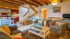 Amplia sala de estar con escalera de madera, cocina al fondo y una zona de estar acogedora.